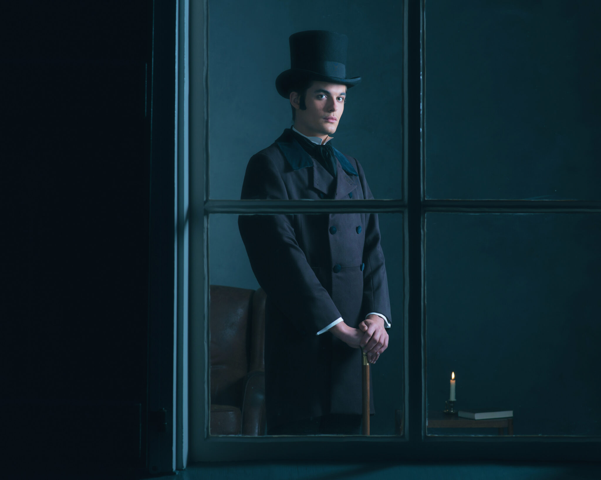 Dickens style man standing with cane behind window.